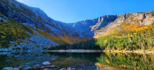 A serene mountain landscape with vibrant autumn foliage reflecting in a calm lake under a clear blue sky.