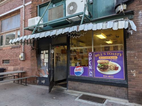 Exterior of Bill's Toasty, a 24-hour burger shop, featuring a colorful sign and a covered entrance.