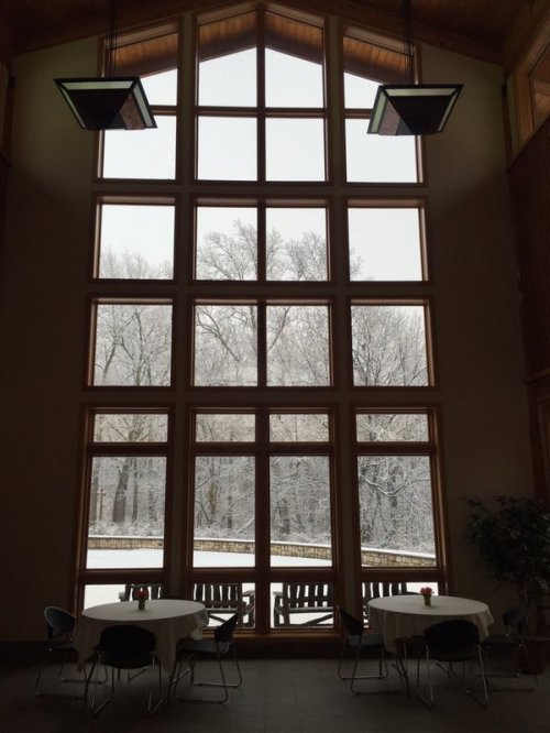 A cozy indoor space with large windows showing a snowy landscape outside, featuring tables and chairs.
