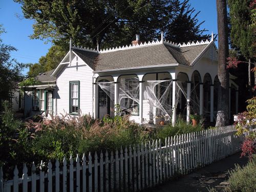 A charming white house with a decorative porch, surrounded by greenery and a white picket fence.