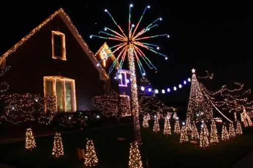 A festive display of colorful Christmas lights on trees and a house, creating a cheerful holiday atmosphere at night.