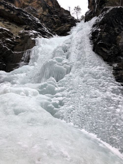 A frozen waterfall cascading down rocky cliffs, surrounded by snow and ice.