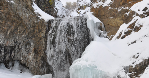A frozen waterfall cascading down rocky cliffs, surrounded by snow and ice.