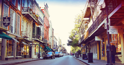 A charming street lined with historic buildings, shops, and balconies, bathed in warm sunlight.