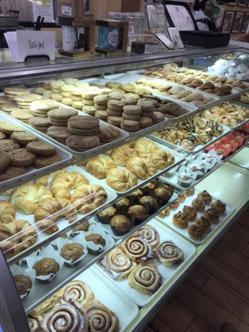 A display case filled with a variety of baked goods, including cookies, pastries, and cinnamon rolls.
