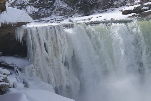 A frozen waterfall cascading over rocky cliffs, surrounded by snow and ice.