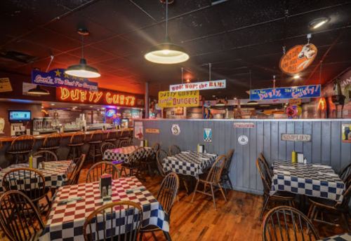 A cozy restaurant interior with checkered tablecloths, colorful signs, and a welcoming bar area.