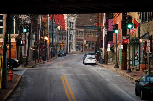 A quiet street scene under an overpass, featuring green traffic lights and shops in the background.