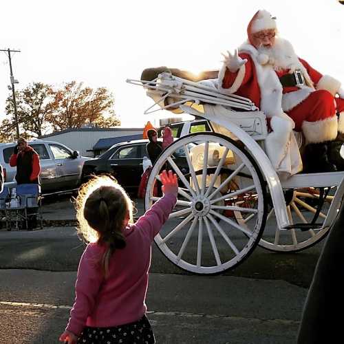 A young girl waves excitedly at Santa Claus, who is riding in a horse-drawn carriage during a festive parade.