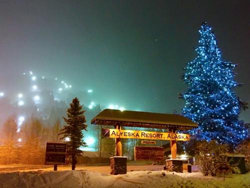 A snowy scene at Alyeska Resort, Alaska, featuring a lit Christmas tree and a sign welcoming visitors.
