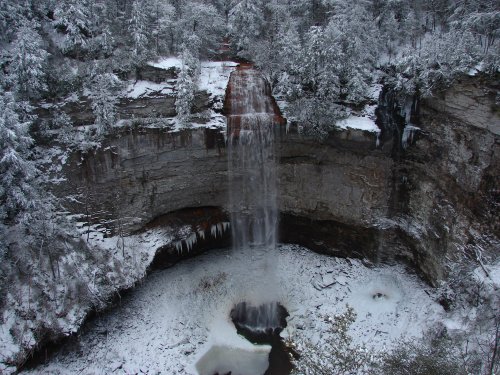 A frozen waterfall surrounded by snow-covered trees and rocky cliffs, creating a serene winter landscape.