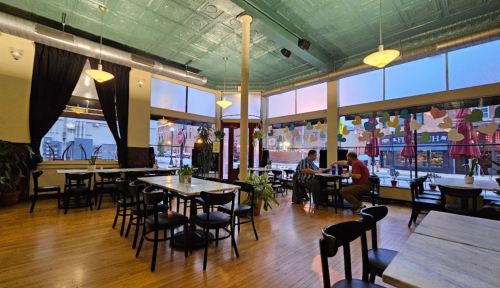 A cozy restaurant interior with wooden floors, green ceiling, and large windows, featuring tables and two patrons.