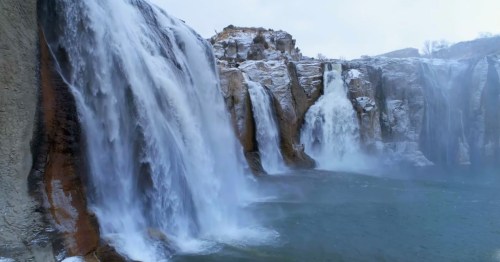 A stunning view of cascading waterfalls surrounded by rocky cliffs and icy terrain.