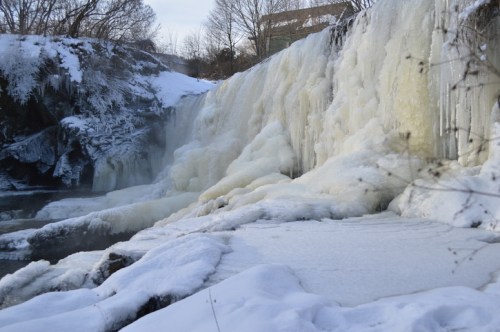 A frozen waterfall surrounded by snow-covered rocks and trees, creating a serene winter landscape.