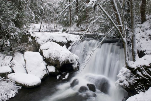 A serene winter scene featuring a waterfall surrounded by snow-covered rocks and trees.