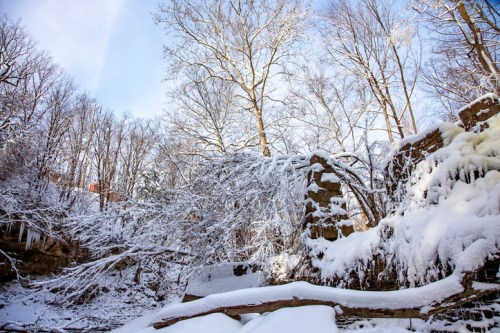 Snow-covered trees and a partially collapsed stone structure in a winter landscape under a clear blue sky.