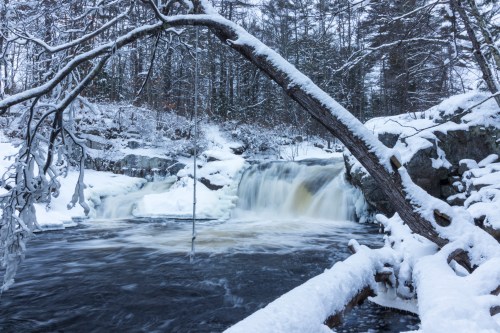 A snowy landscape featuring a waterfall surrounded by trees and ice, creating a serene winter scene.