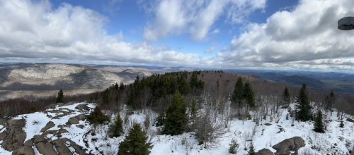 A panoramic view of snow-covered mountains and trees under a cloudy sky.