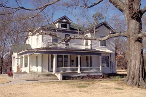 A large, two-story white house with a green roof, surrounded by bare trees and a grassy lawn on a clear day.