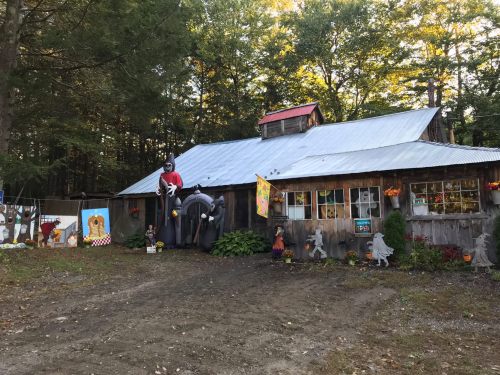 A rustic wooden building surrounded by trees, decorated with colorful banners and Halloween decorations.