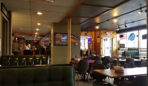 Interior of a casual restaurant with green booths, wooden decor, and a bar area in the background.