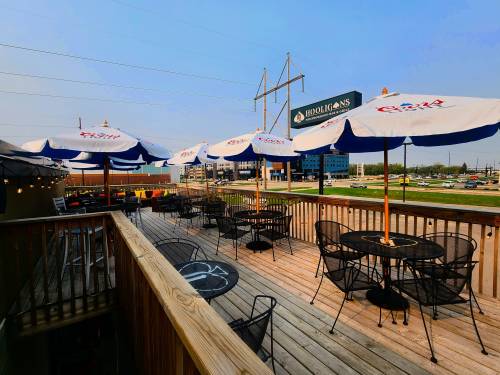 Outdoor patio with tables and umbrellas, overlooking a parking lot and buildings in the background.