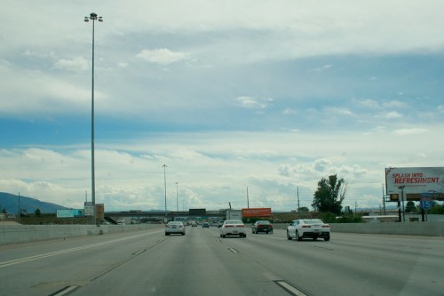 A view of a busy highway with cars, under a cloudy sky and a billboard advertising refreshments.