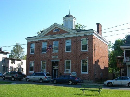 Historic brick building with a cupola, labeled "Whitesboro Town Hall," surrounded by cars and greenery.