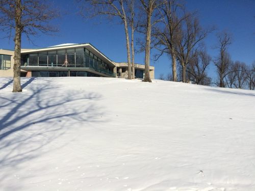 A modern building on a snowy hillside, surrounded by bare trees under a clear blue sky.