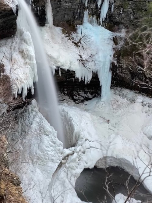A frozen waterfall cascading over icy cliffs into a snowy landscape below.