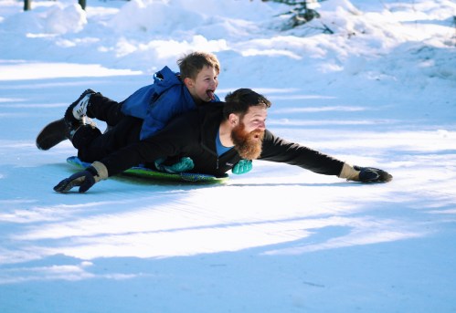A man and a child sledding down a snowy hill, both smiling and enjoying the winter day.