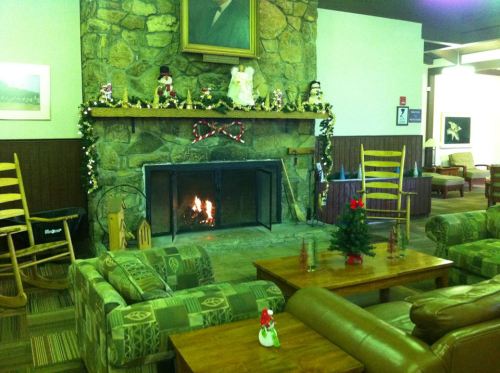 Cozy lounge with a stone fireplace, decorated mantel, festive decor, and comfortable seating.