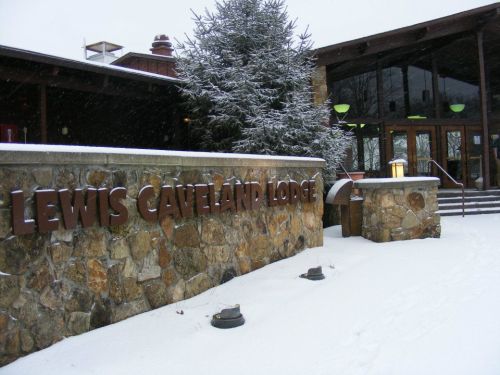 Snow-covered entrance of Lewis Cavernland Lodge with stone signage and a tree in the background.