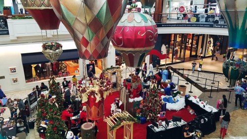 A festive mall scene with large holiday decorations, a Christmas tree, and people enjoying seasonal activities.