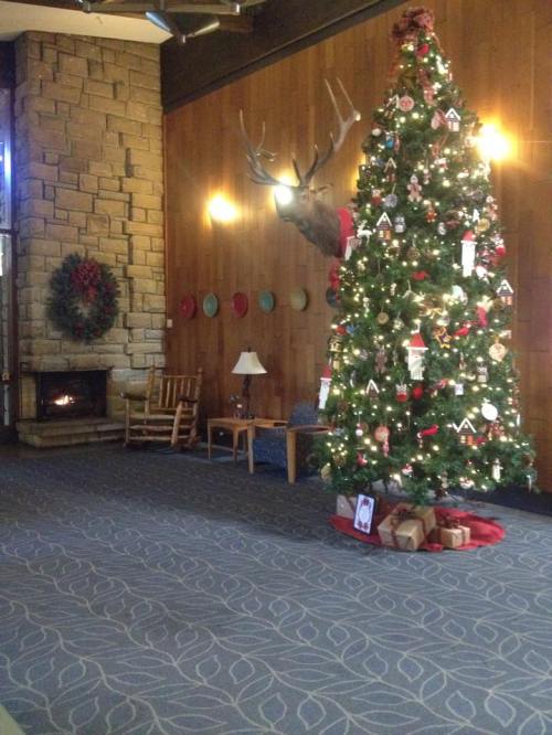 Cozy lobby with a decorated Christmas tree, fireplace, and rustic decor, featuring a stone wall and wooden accents.