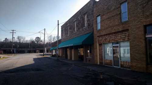 A quiet street scene featuring brick buildings with awnings and a clear blue sky.