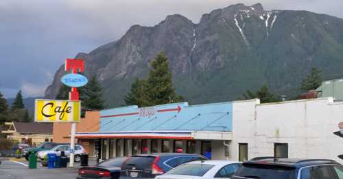 A café building with a colorful sign, set against a backdrop of mountains under a cloudy sky.