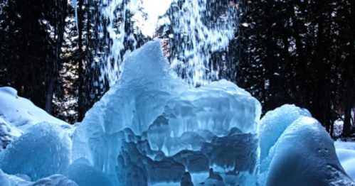 A stunning ice formation with cascading water, surrounded by snow and trees, creating a serene winter scene.