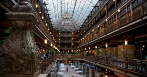 A grand indoor atrium with ornate architecture, glass ceiling, and balconies, featuring tables below.