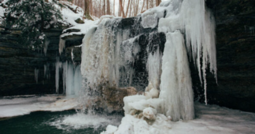 A frozen waterfall surrounded by icy rocks and snow-covered trees in a winter landscape.