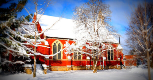A red brick church surrounded by snow-covered trees on a bright winter day.