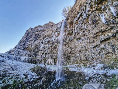 A stunning waterfall cascading down a rocky cliff, surrounded by icicles and a clear blue sky.