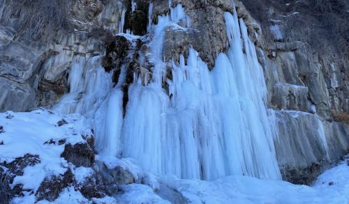 A frozen waterfall cascading down a rocky cliff, surrounded by snow and ice.