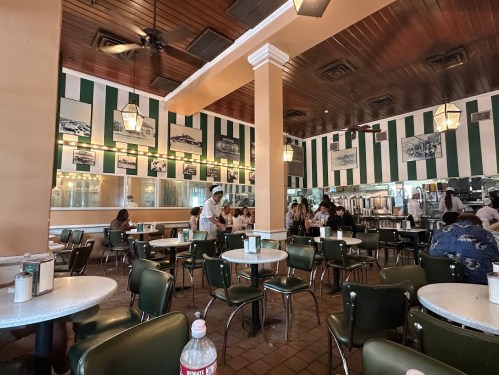 A retro diner interior with green and white striped walls, round tables, and patrons enjoying their meals.
