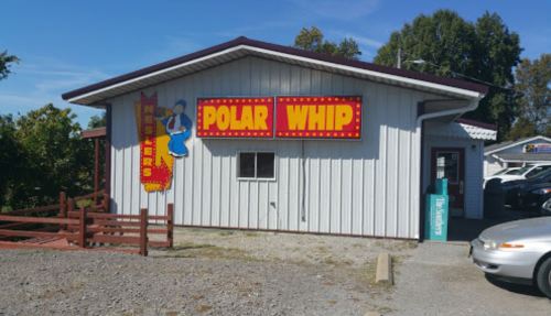 A white building with a red and yellow "Polar Whip" sign, featuring a cartoon character, surrounded by gravel and trees.