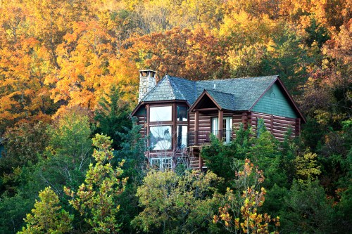A cozy log cabin surrounded by vibrant autumn foliage in a serene forest setting.