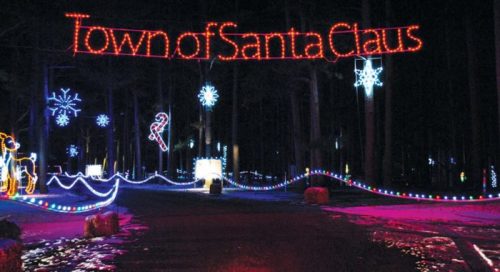 Colorful holiday lights illuminate a pathway with a sign reading "Town of Santa Claus" and festive decorations.