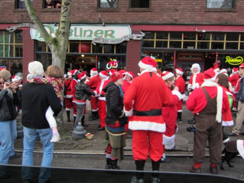 A crowd of people dressed as Santa Claus gathers outside a pub, celebrating in festive attire.