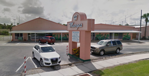 A pink building with a sign reading "Marge's" and parked cars in front, set in a sunny outdoor environment.