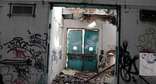 A view through a doorway in an abandoned building, with graffiti on the walls and debris on the floor.